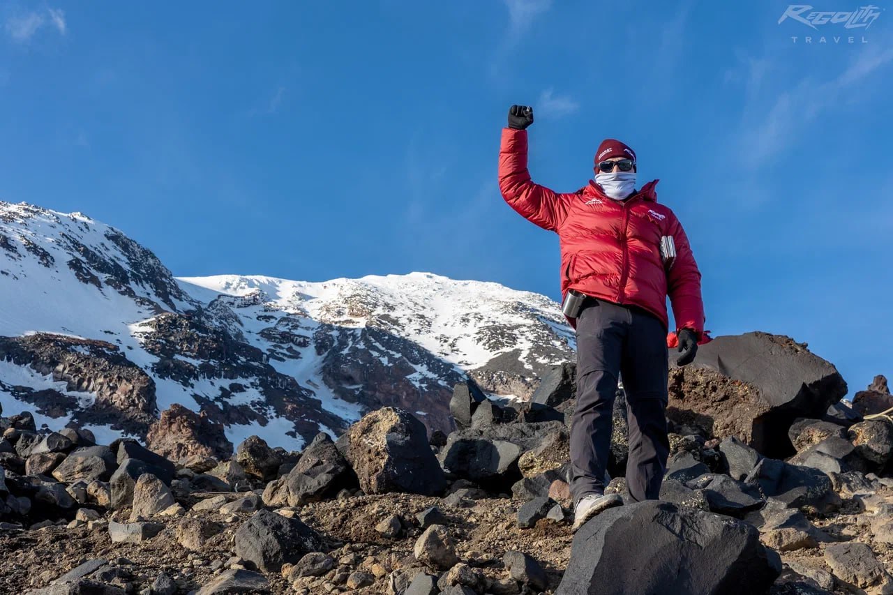 A Regolith Travel climber on the slopes of Mount Ararat, fist raised in a victory pose, summer 2025.