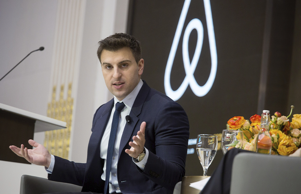 Брайан Чески, сооснователь и CEO Airbnb, выступает на сцене на фоне логотипа компании
