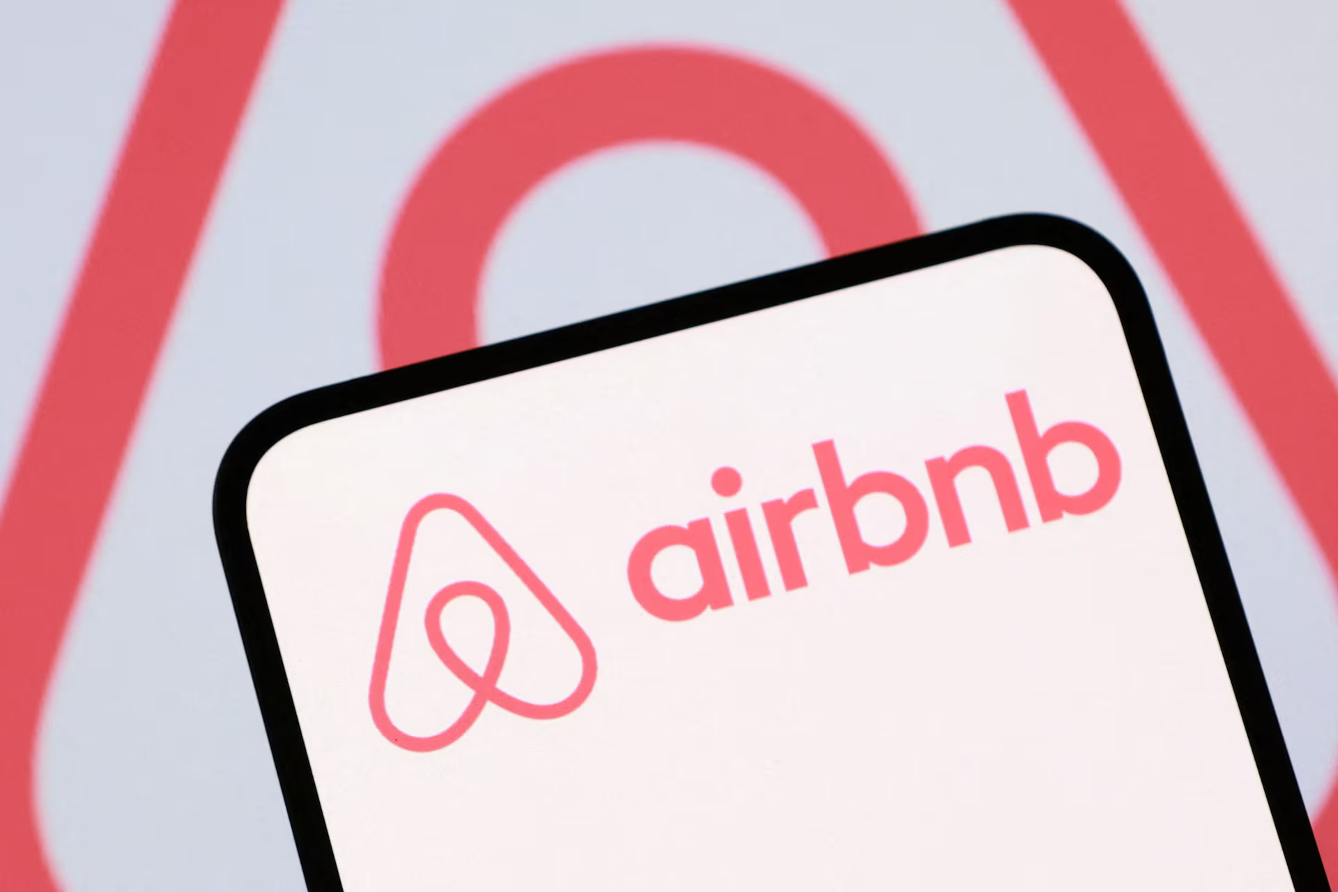 Логотип Airbnb на экране смартфона на фоне фирменного символа компании