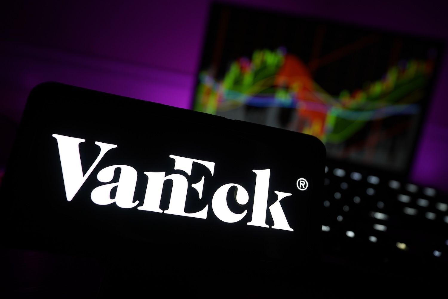 The VanEck logo on a smartphone screen against a stock chart background.