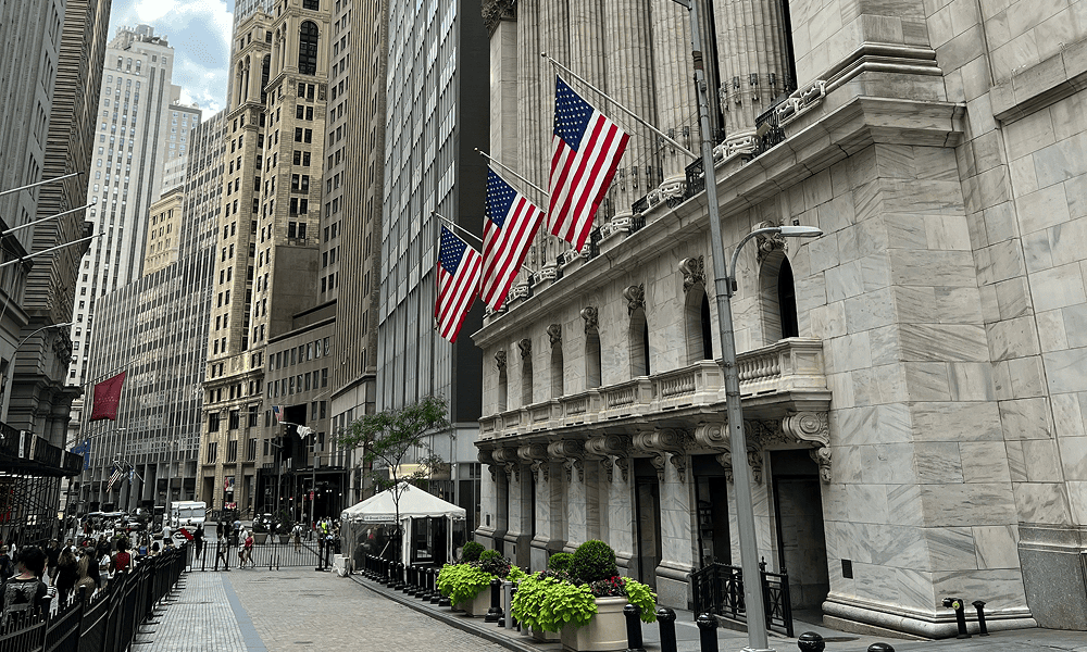 Нью-Йоркская фондовая биржа (NYSE) на Уолл-стрит с американскими флагами на фасаде.