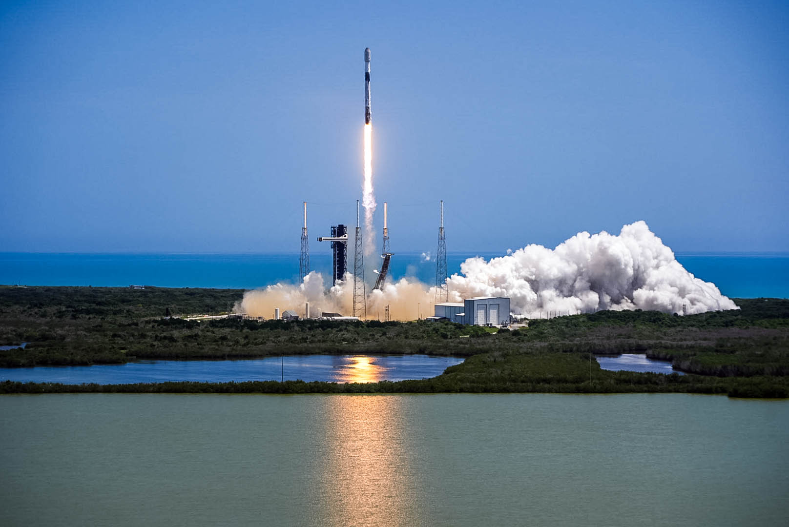 Ракета SpaceX стартует с площадки на побережье, оставляя за собой яркий огненный след и облако дыма.
