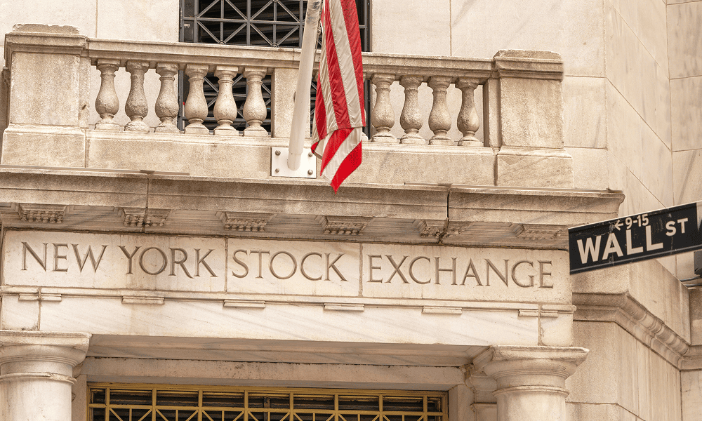 Фасад Нью-Йоркской фондовой биржи с американским флагом и указателем Wall Street.