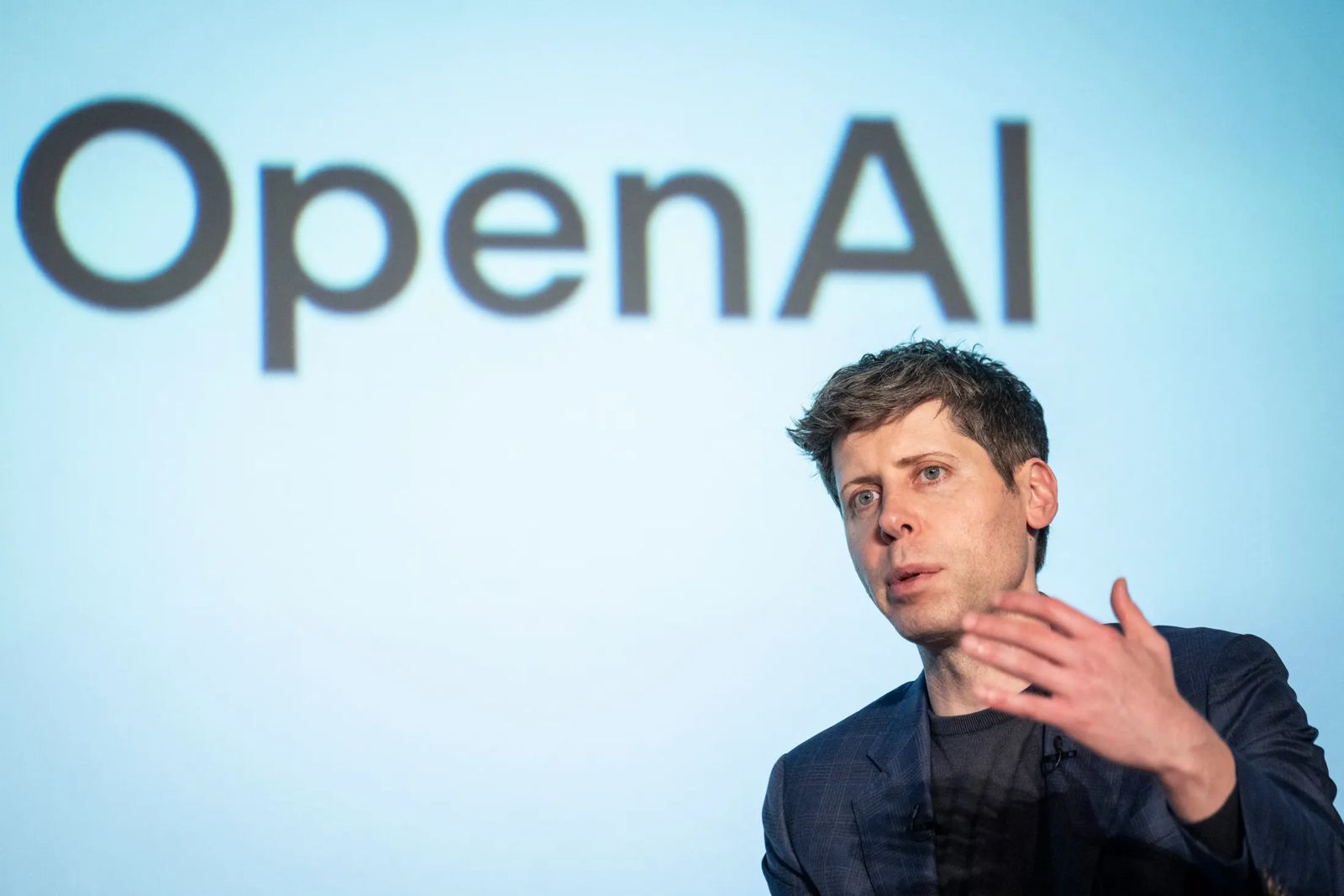 Выступление на сцене на фоне крупного логотипа OpenAI.