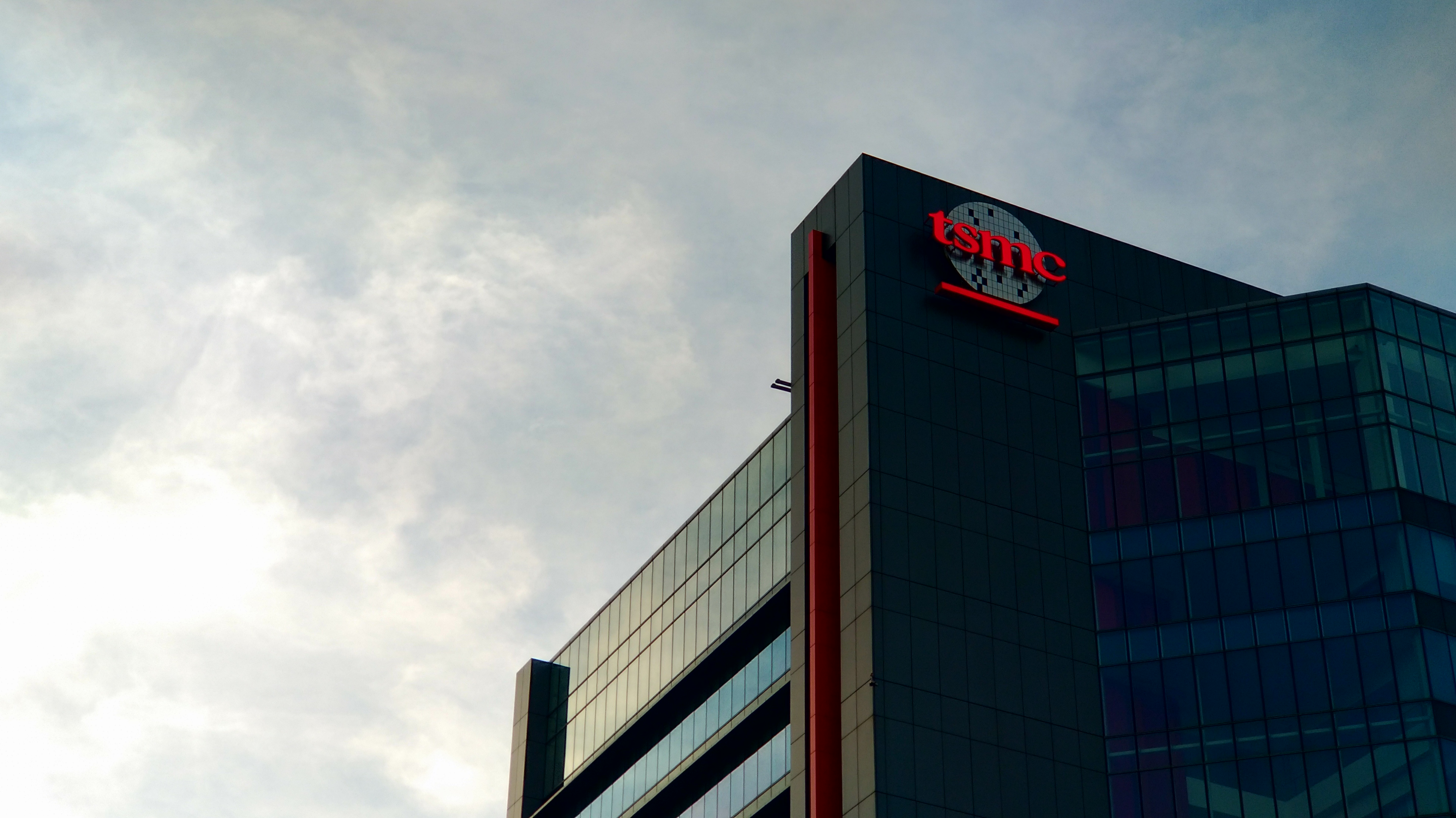 Красный логотип TSMC на темном стеклянном фасаде фабрики.