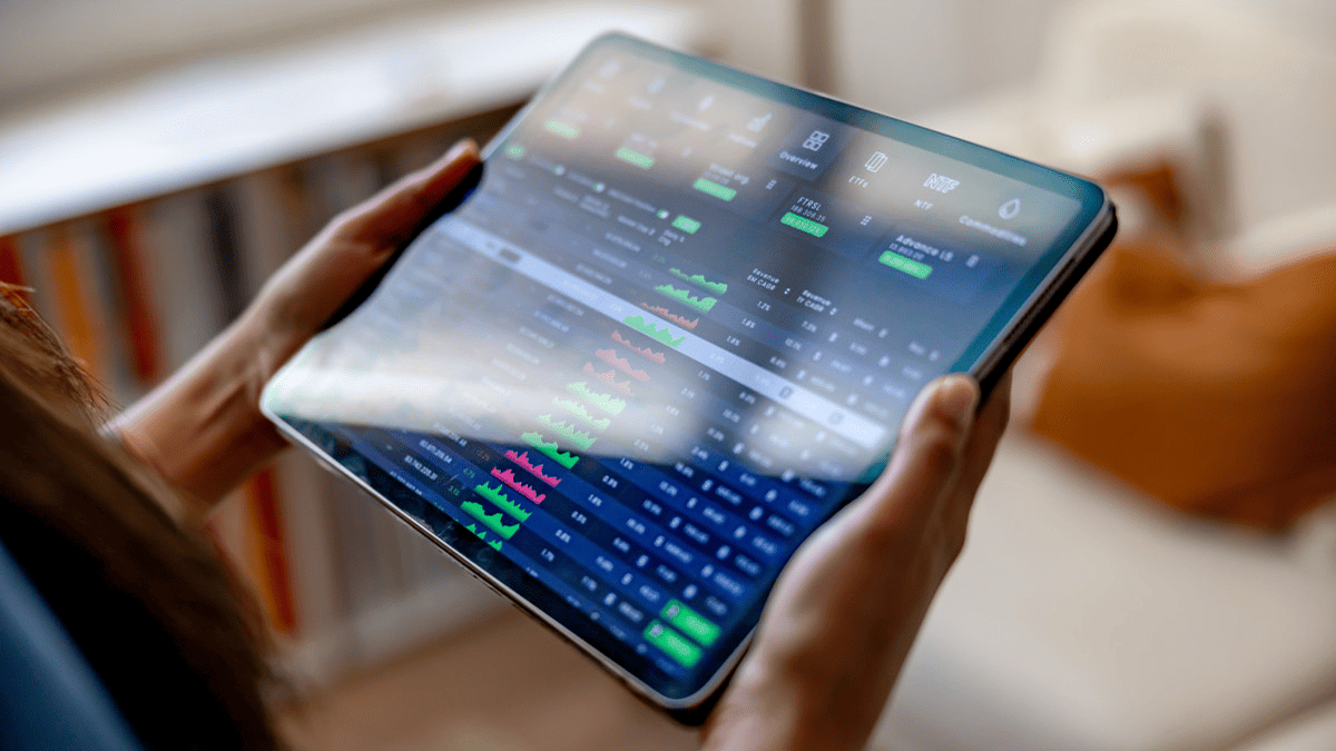 Hands holding a tablet with a financial dashboard – charts, prices, and market analytics.